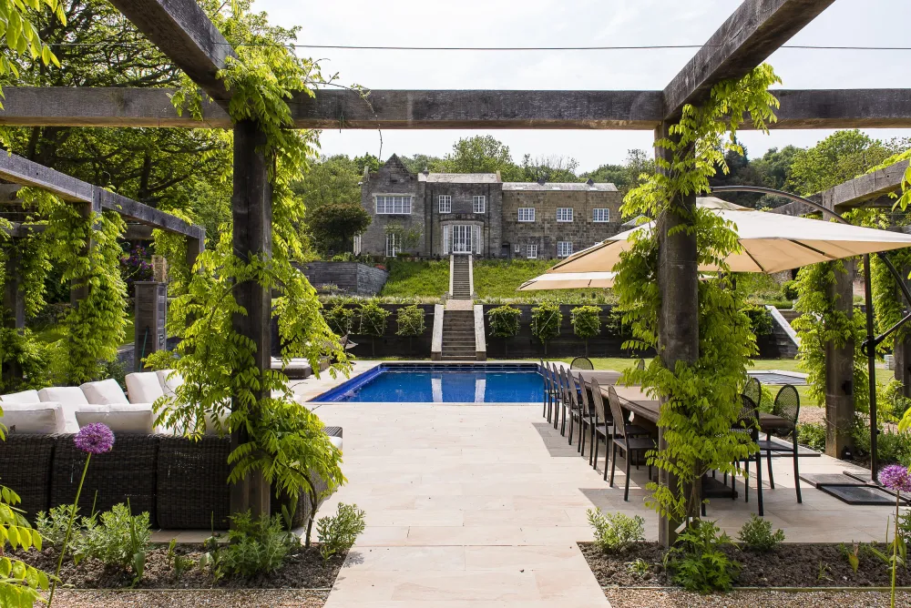 Pool surrounded by terrace, framed through wisteria-clad oak pergola